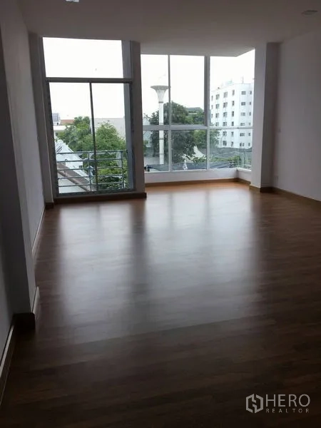 Home Office for sale in Lat Phrao, Bangkok - Corner workspace with floor-to-ceiling glass and views of city greenery.