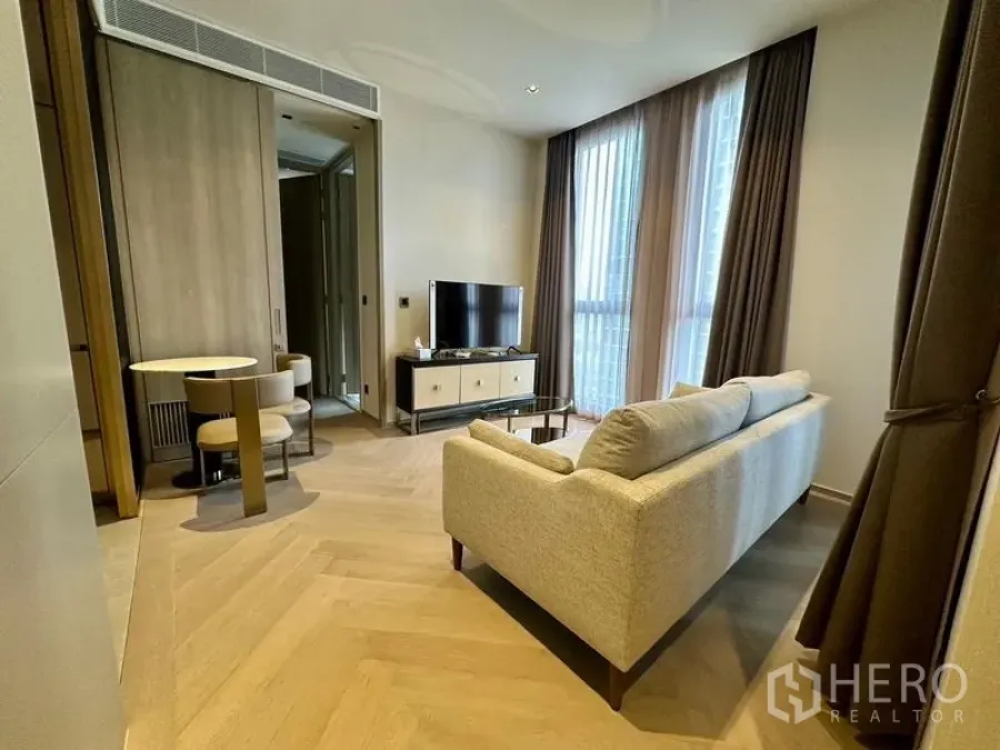 Condominium for rent - Living room angle showing sofa, TV stand, tall curtains, and herringbone wood flooring.