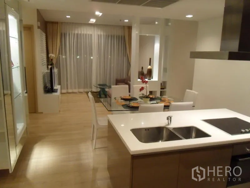 Condominium for rent in Khlong Toei, Bangkok - Open-plan kitchen with island sink and cooktop facing the dining and living space.