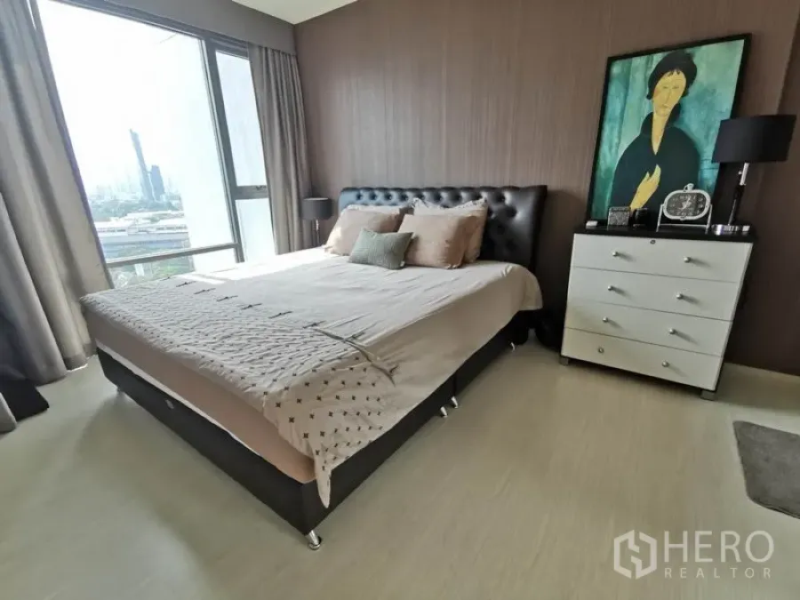Condominium for rent in Khlong Toei, Bangkok - Bright bedroom with large window, upholstered bed, side lamps and dresser overlooking the city.