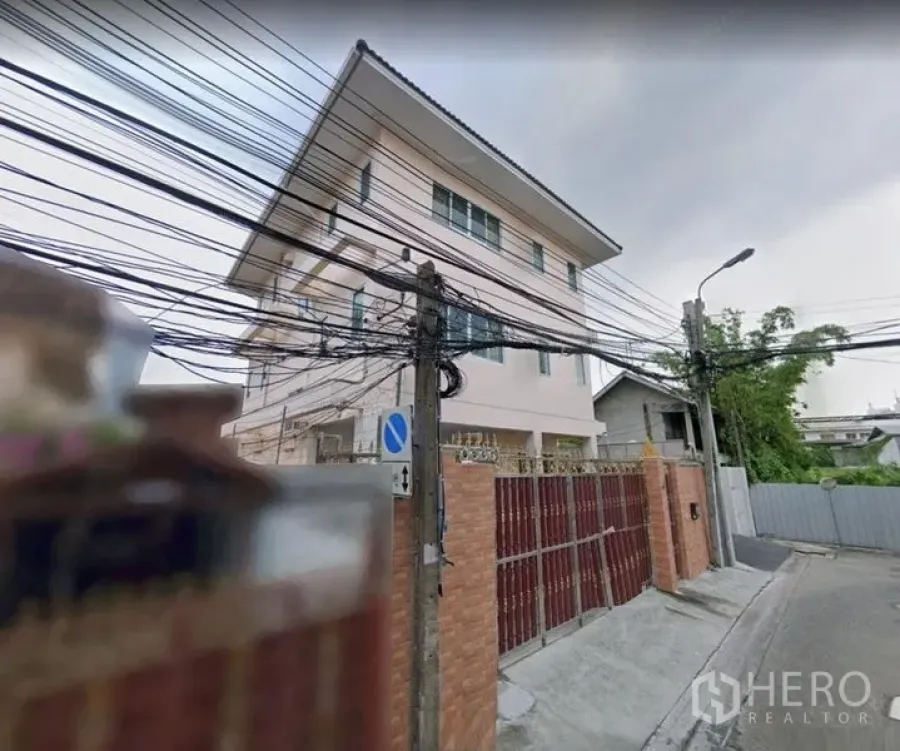 Detached House for rent in Khlong Toei, Bangkok - Corner exterior of the house with tall gate along a quiet residential street.