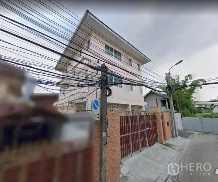 Detached House for rent in Khlong Toei, Bangkok - Corner exterior of the house with tall gate along a quiet residential street.