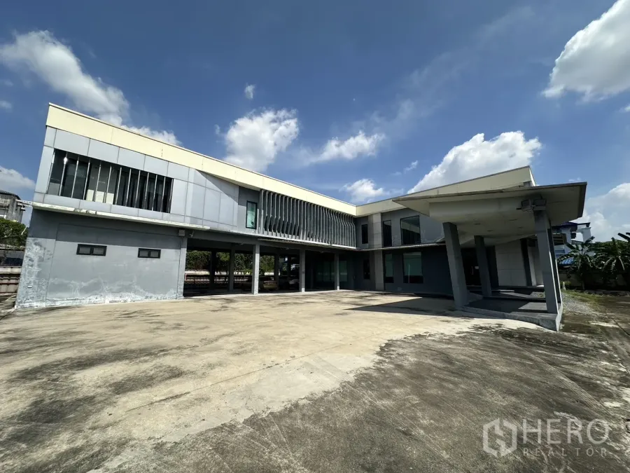 带办公室的家 出租在Prawet, Bangkok - 两层办公楼正立面与宽阔停车区，蓝天下景观。
