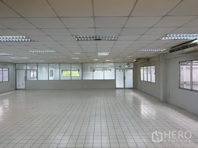 Factory for rent in Nonthaburi - Bright tiled office space with suspended ceiling and glass partitions.