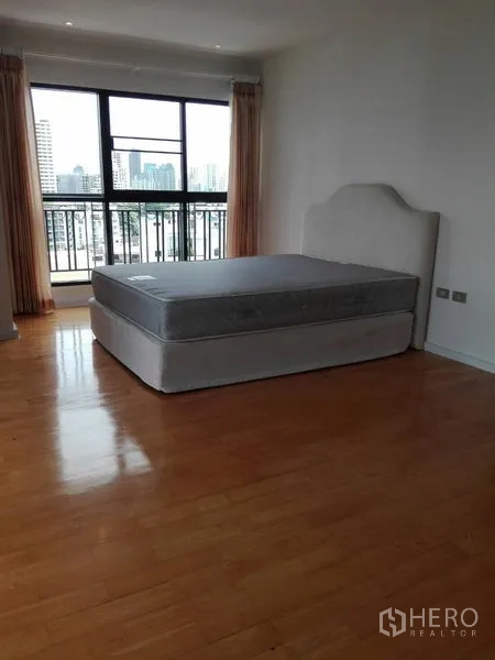 Condominium for rent in Khlong Toei, Bangkok - Bedroom with city views through large window and balcony railings, wood flooring and a bed.