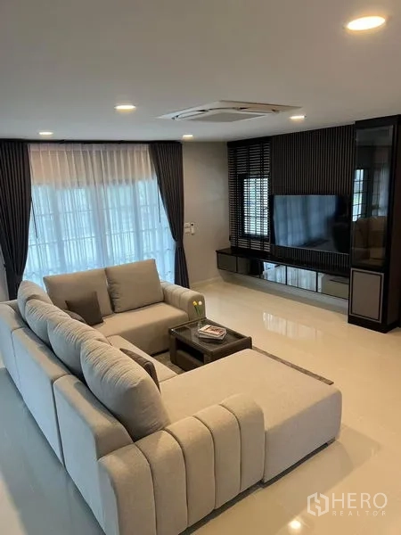 独立式住宅 出租在Bang Phli, Samut Prakan - 客厅另一视角，转角沙发朝向电视墙，深色窗帘。
