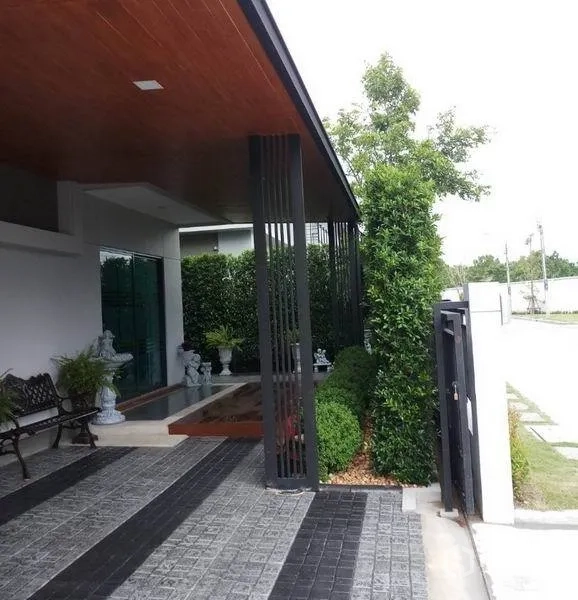 独立式住宅 出售在Nonthaburi - 前门门廊，挑檐屋顶与竖向金属立柱，修剪灌木。