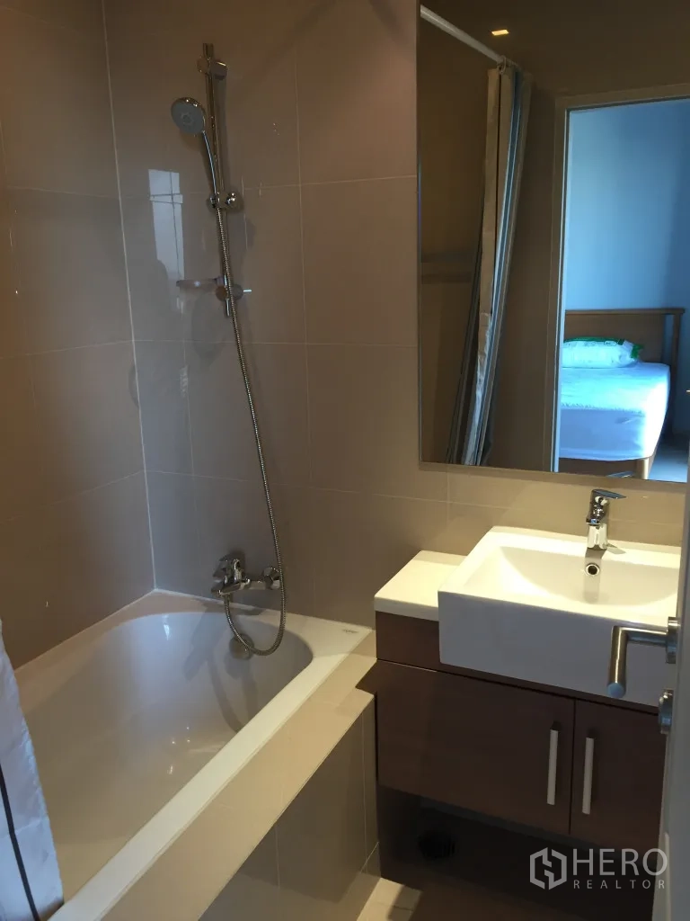 Condominium for rent in Bangkok - Bathroom with bathtub, handheld shower, vanity, and large mirror.