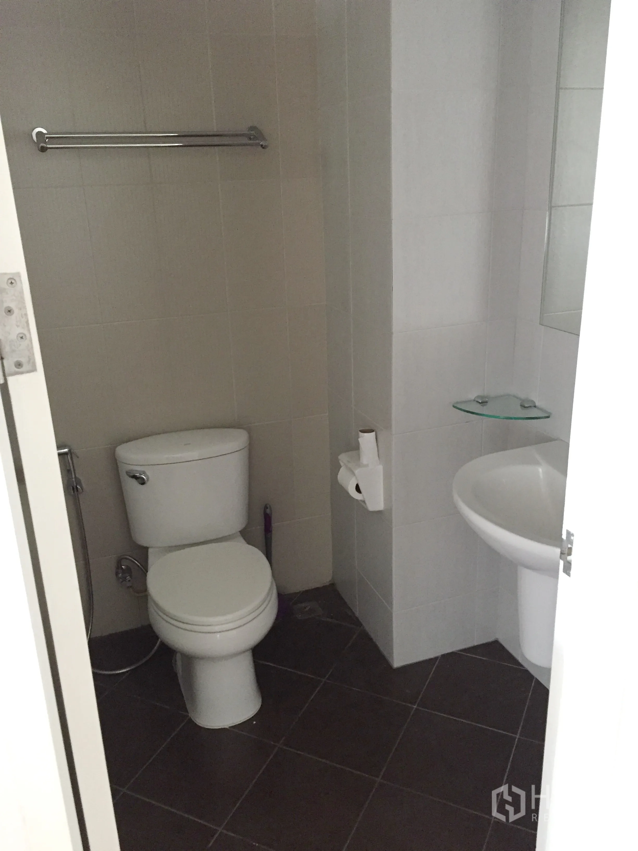 Condominium for rent in Khlong Toei, Bangkok - Tiled bathroom with toilet, pedestal sink and towel bar in a compact layout.