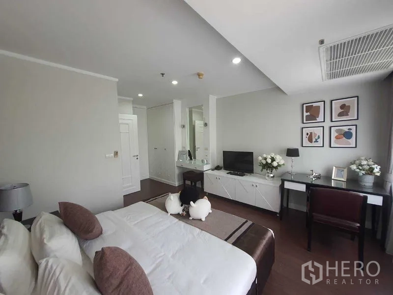 房间 出租在Watthana, Bangkok - 宽敞卧室，展示床、梳妆区、收纳柜与柔和灯光。