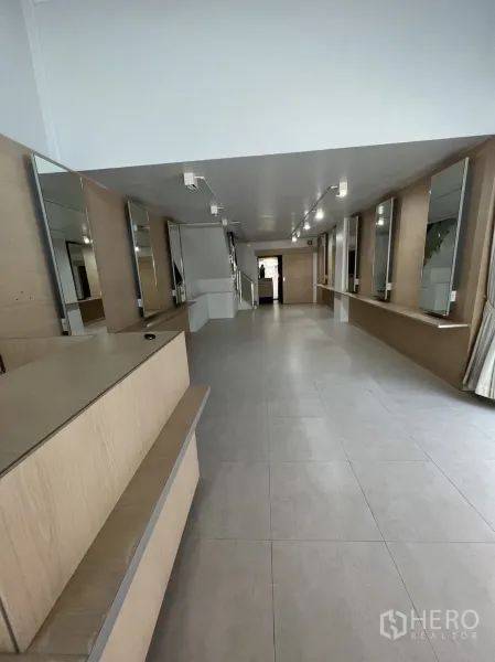 Shophouse for rent in Watthana, Bangkok - Long ground-floor retail space with light-wood counters, mirrors and tiled flooring.