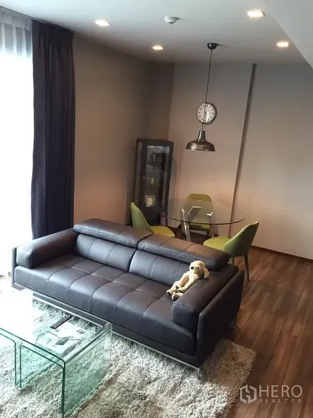 Condominium for rent in Watthana, Bangkok - Cozy living area with a leather sofa, glass coffee table, and round dining set beneath a pendant light.