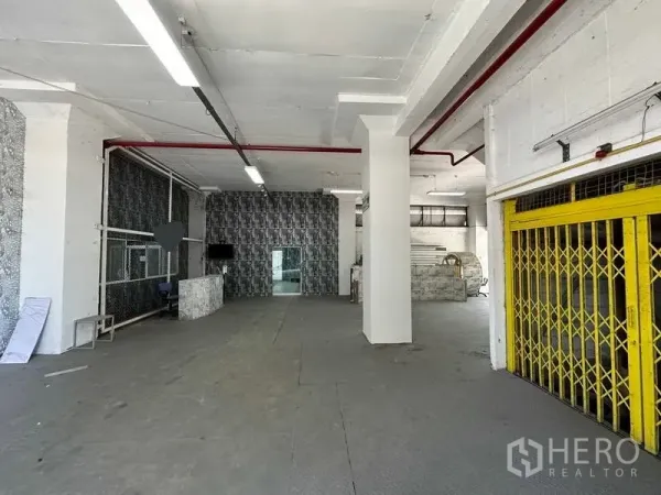 工厂 出租在Mueang Samut Prakan, Samut Prakan - 宽阔厂房大厅，配黄色折叠闸门、顶置照明与红色消防管。