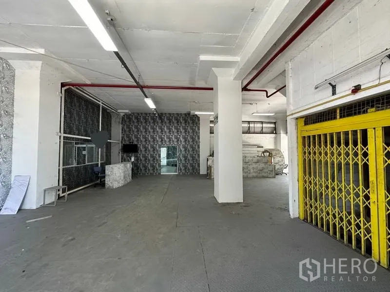 工厂 出租在Mueang Samut Prakan, Samut Prakan - 宽阔厂房大厅，配黄色折叠闸门、顶置照明与红色消防管。