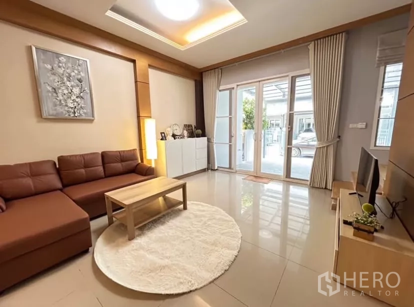 联排别墅 出租在Wang Thonglang, Bangkok - 客厅明亮，L形皮沙发、电视柜与落地推拉门