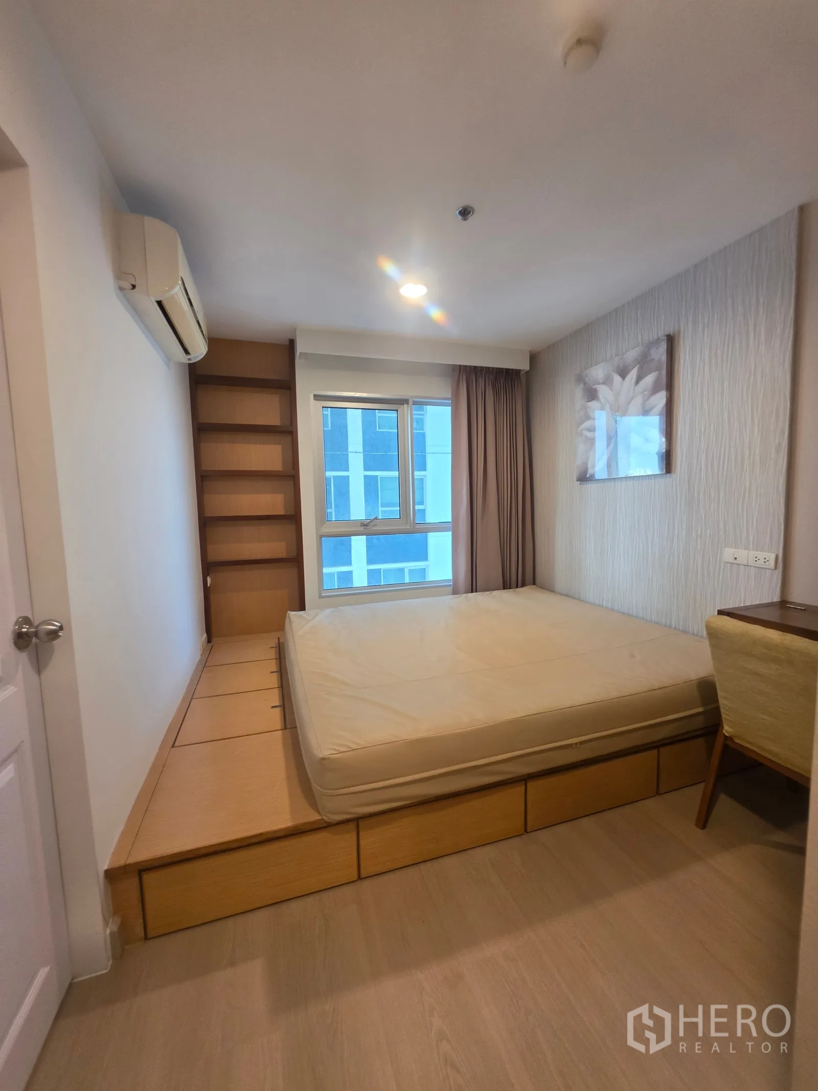 Condominium for rent in Huai Khwang, Bangkok - Wide view of bedroom with storage drawers under platform bed and shelving.