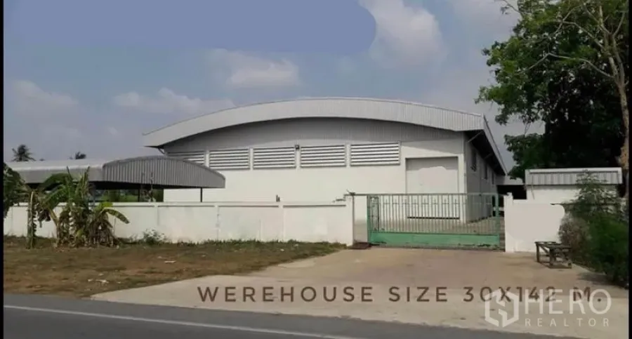 Warehouse for rent or sale - Front view of a modern white warehouse with curved roof, gated entrance and roadside access.