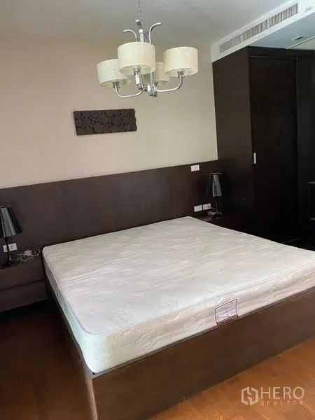 Condominium for rent in Khlong Toei, Bangkok - Bedroom with queen bed, wood furniture, built-in wardrobe, bedside lamps and chandelier.