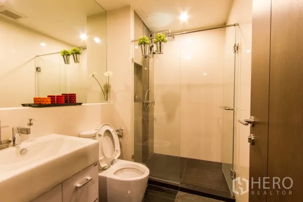 Condominium for rent or sale in Sathon, Bangkok - Clean bathroom featuring a large mirror, vanity, toilet and a glass-enclosed walk-in shower.