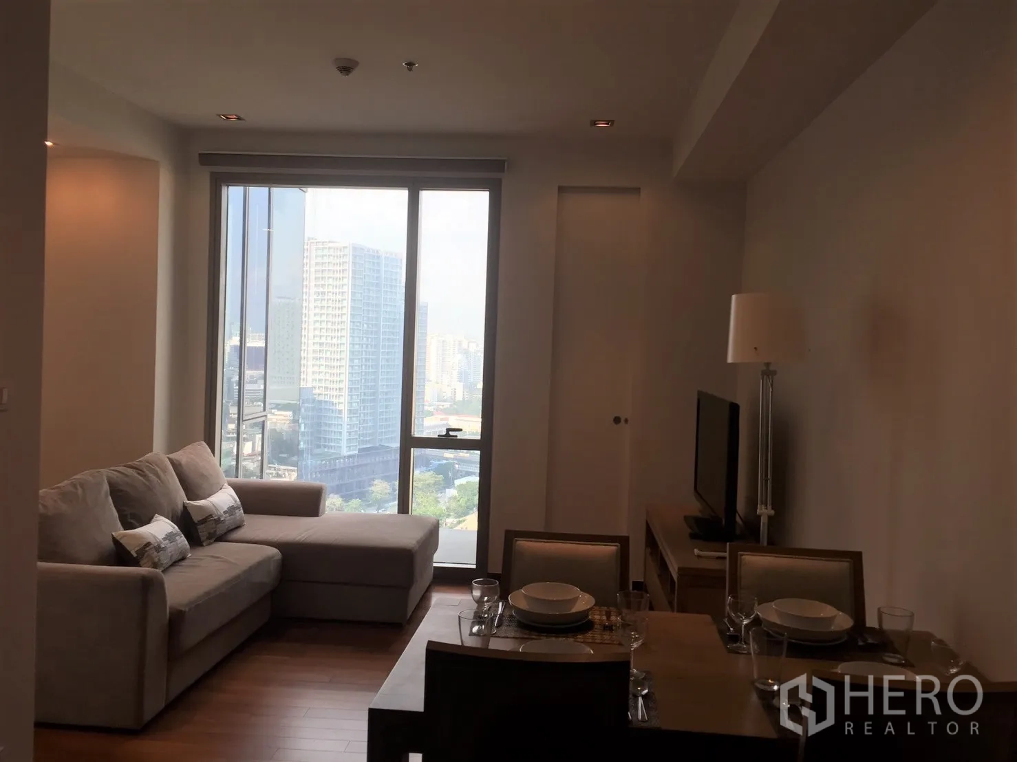 Condominium for rent in Khlong Toei, Bangkok - Bright living and dining area with sofa, TV and floor-to-ceiling window overlooking the Bangkok skyline.