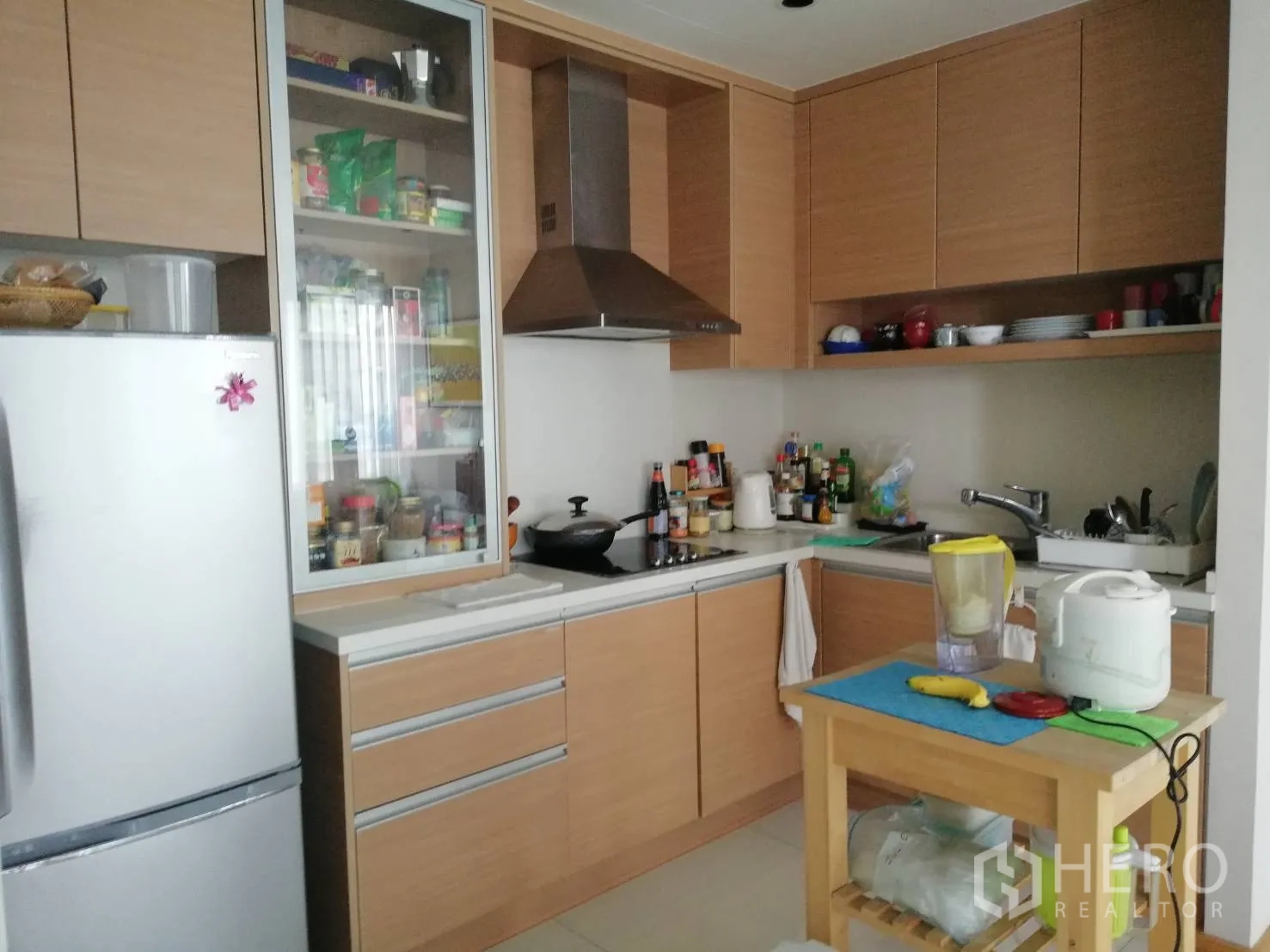 Condominium for sale in Khlong Toei, Bangkok - U-shaped kitchen with wood cabinetry, range hood and full-size fridge.