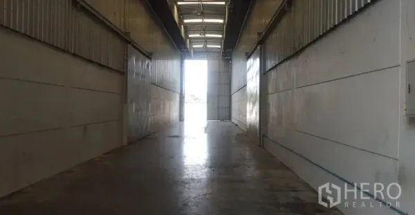 Warehouse for rent in Pathum Thani - Industrial passage with concrete floor and roll-up doors opening to exterior light.