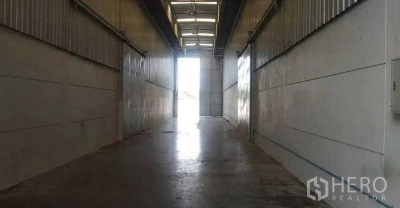 Warehouse for rent in Pathum Thani - Industrial passage with concrete floor and roll-up doors opening to exterior light.