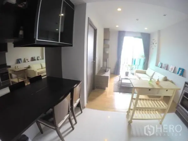 Condominium for rent in Khlong Toei, Bangkok - Open-plan dining and living area with black dining table, rolling island and sliding doors to the balcony.