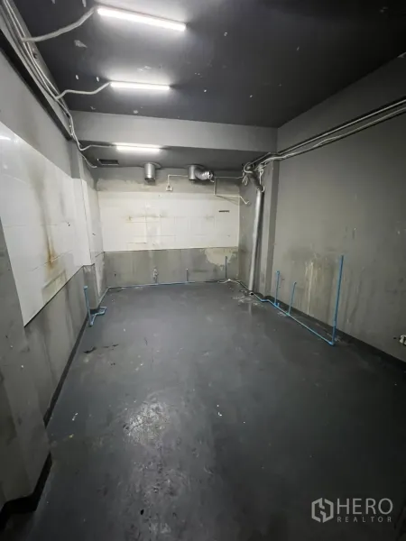 Shophouse for rent in Watthana, Bangkok - Ventilated prep room with exposed piping, grey walls and bright strip lights.