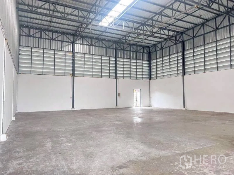 Warehouse for rent in Lam Luk Ka, Pathum Thani - Spacious warehouse bay with metal roof, concrete floor, and a side door.