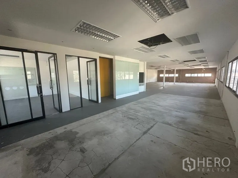 Warehouse for rent in Saphan Sung, Bangkok - Expansive office floor with glass rooms and mixed concrete and carpet flooring.