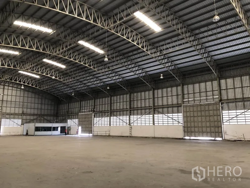 货栈 出租在Pathum Thani - 室内侧面视角，成排卷帘门、高棚灯与通风百叶。