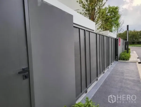 独立式住宅 出租在Saphan Sung, Bangkok - 房屋正前方的灰色金属推拉大门与行人侧门，沿整洁的人行道而设。
