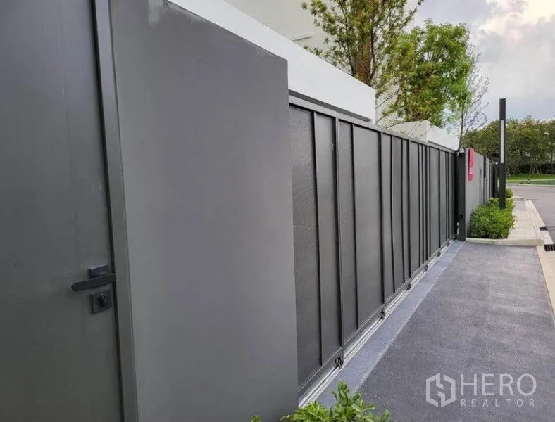独立式住宅 出租在Saphan Sung, Bangkok - 房屋正前方的灰色金属推拉大门与行人侧门，沿整洁的人行道而设。