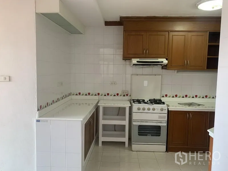 公寓 出租在Watthana, Bangkok - 封闭式厨房，木质橱柜，白色墙砖，带排烟机的燃气灶与L型台面。