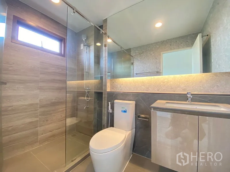 Detached House for rent in Bang Kapi, Bangkok - Contemporary bathroom with glass-enclosed shower, large mirror and vanity.