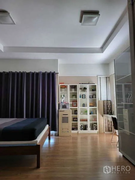 独立式住宅 出租在Lat Krabang, Bangkok - 明亮卧室，平台床、玻璃门书柜与窗边书桌，木地板和深色窗帘。
