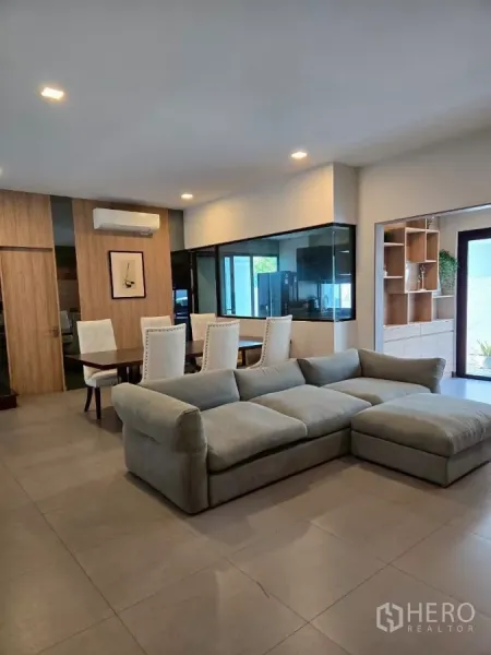 联排别墅 出租在Bang Phli, Samut Prakan - 现代联排别墅的开放式客餐厅，灰色转角沙发、餐桌与玻璃隔断厨房。