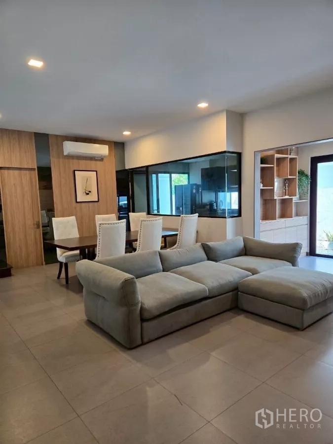 联排别墅 出租在Bang Phli, Samut Prakan - 现代联排别墅的开放式客餐厅，灰色转角沙发、餐桌与玻璃隔断厨房。