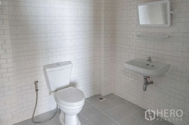 Warehouse for rent in Khlong Luang, Pathum Thani - Clean tiled restroom with toilet, wall mirror, sink and spray hose.