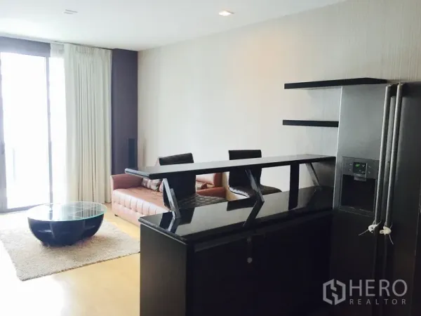 Condominium for rent or sale in Khlong Toei, Bangkok - Living area with bar counter, sofa seating and large sliding glass doors beside a stainless refrigerator.