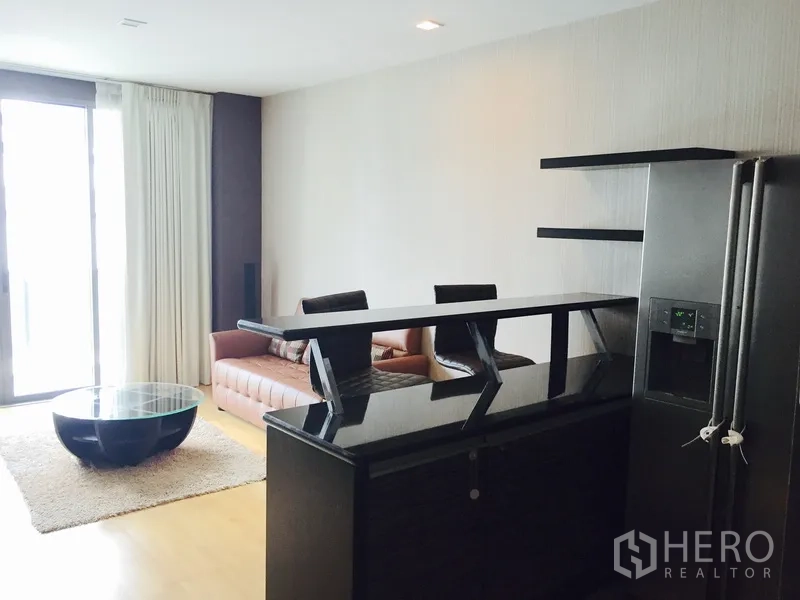 Condominium for rent or sale in Khlong Toei, Bangkok - Living area with bar counter, sofa seating and large sliding glass doors beside a stainless refrigerator.
