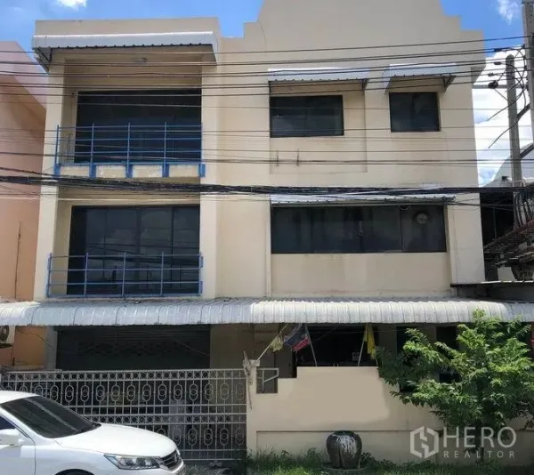 โรงงาน ขายในBang Bua Thong, Nonthaburi - อาคารโรงงานสูงสามชั้นสีครีม ราวเหล็กสีน้ำเงิน หน้าบ้านมีหลังคากันสาด พร้อมประตูรั้วและที่จอดรถ ในบางบัวทอง นนทบุรี