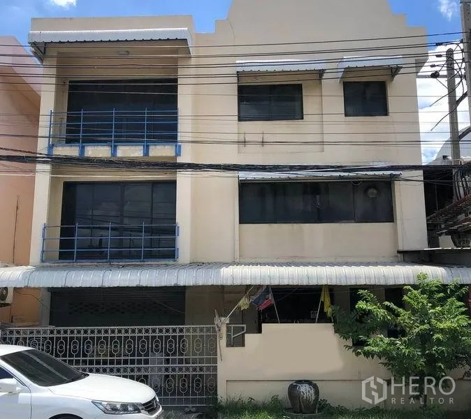 โรงงาน ขายในBang Bua Thong, Nonthaburi - อาคารโรงงานสูงสามชั้นสีครีม ราวเหล็กสีน้ำเงิน หน้าบ้านมีหลังคากันสาด พร้อมประตูรั้วและที่จอดรถ ในบางบัวทอง นนทบุรี