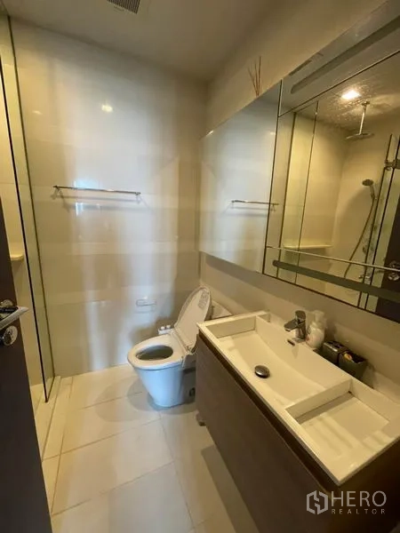 Condominium for rent in Khlong Toei, Bangkok - Contemporary bathroom with vanity, mirrored cabinet, toilet and glass-enclosed shower.