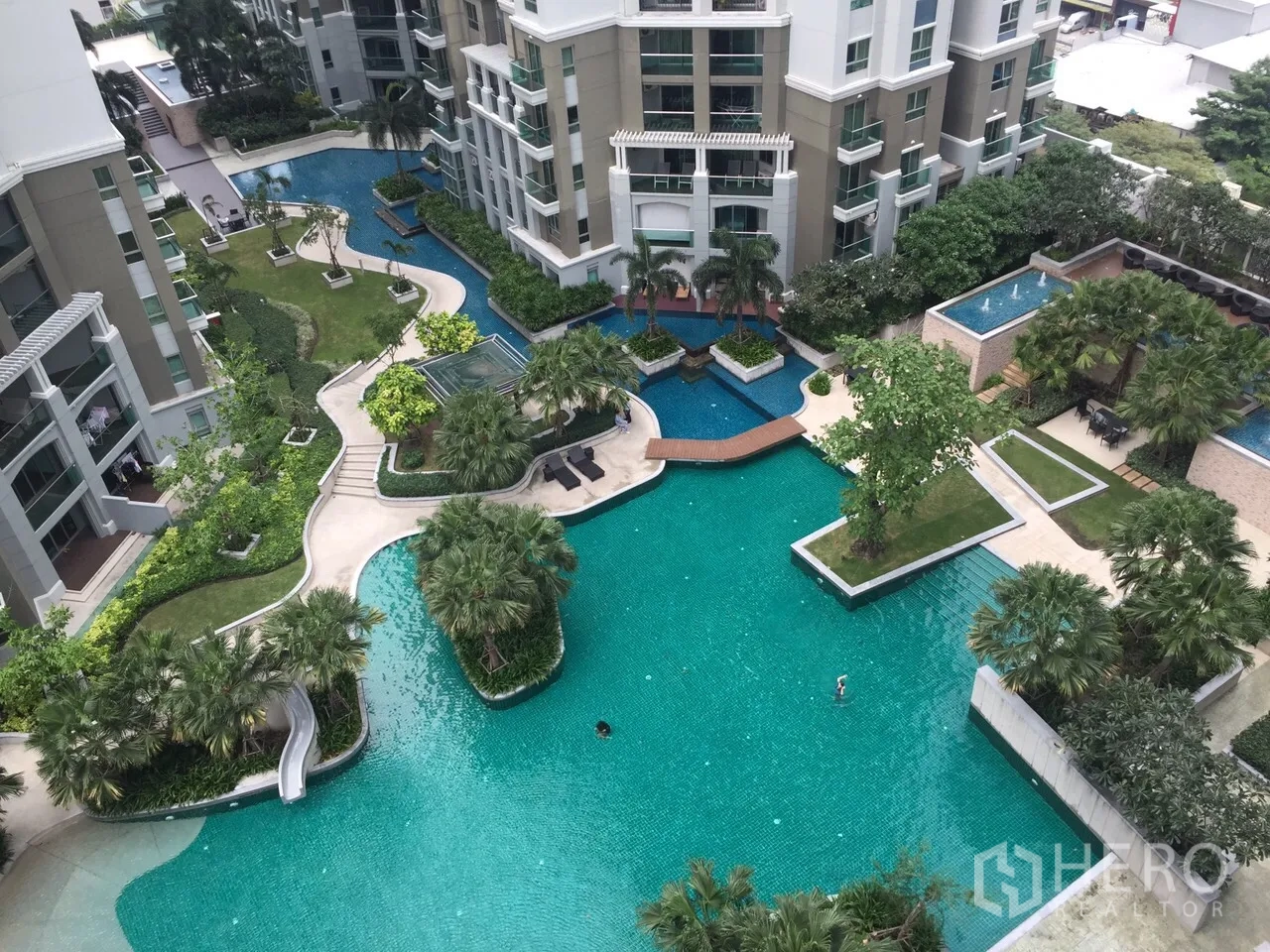 คอนโด ให้เช่าในHuai Khwang, Bangkok - ภาพมุมสูงของสระว่ายน้ำสไตล์ลากูน พื้นที่สวน และสะพานเชื่อม ท่ามกลางอาคารคอนโดโมเดิร์น
