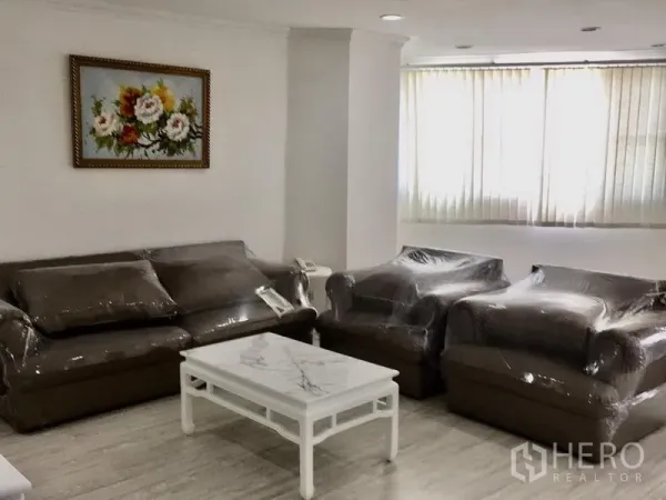 公寓 出租在Watthana, Bangkok - 客厅角落放置包膜的沙发与单椅，大理石面茶几，落地窗配百叶帘。