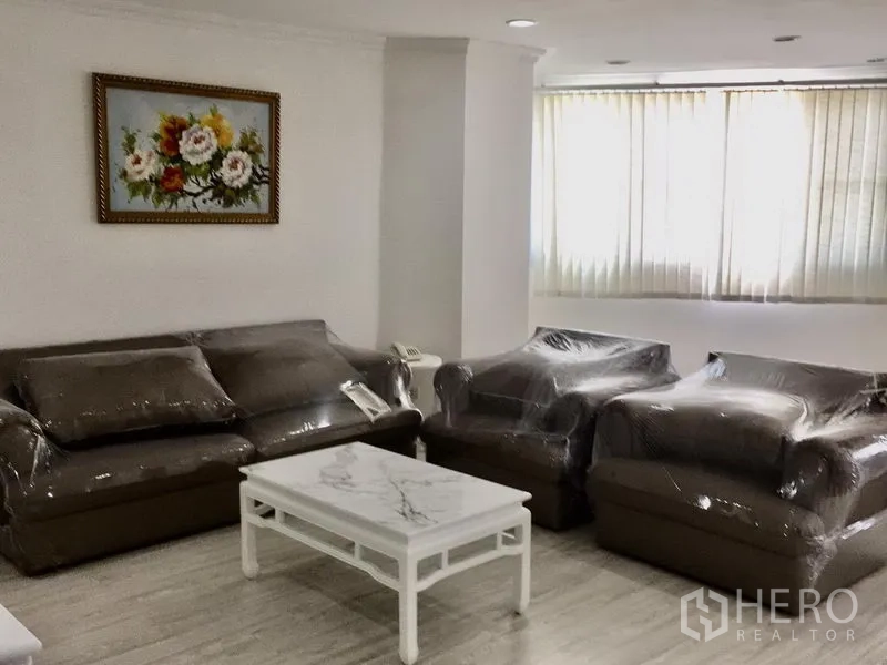 公寓 出租在Watthana, Bangkok - 客厅角落放置包膜的沙发与单椅，大理石面茶几，落地窗配百叶帘。