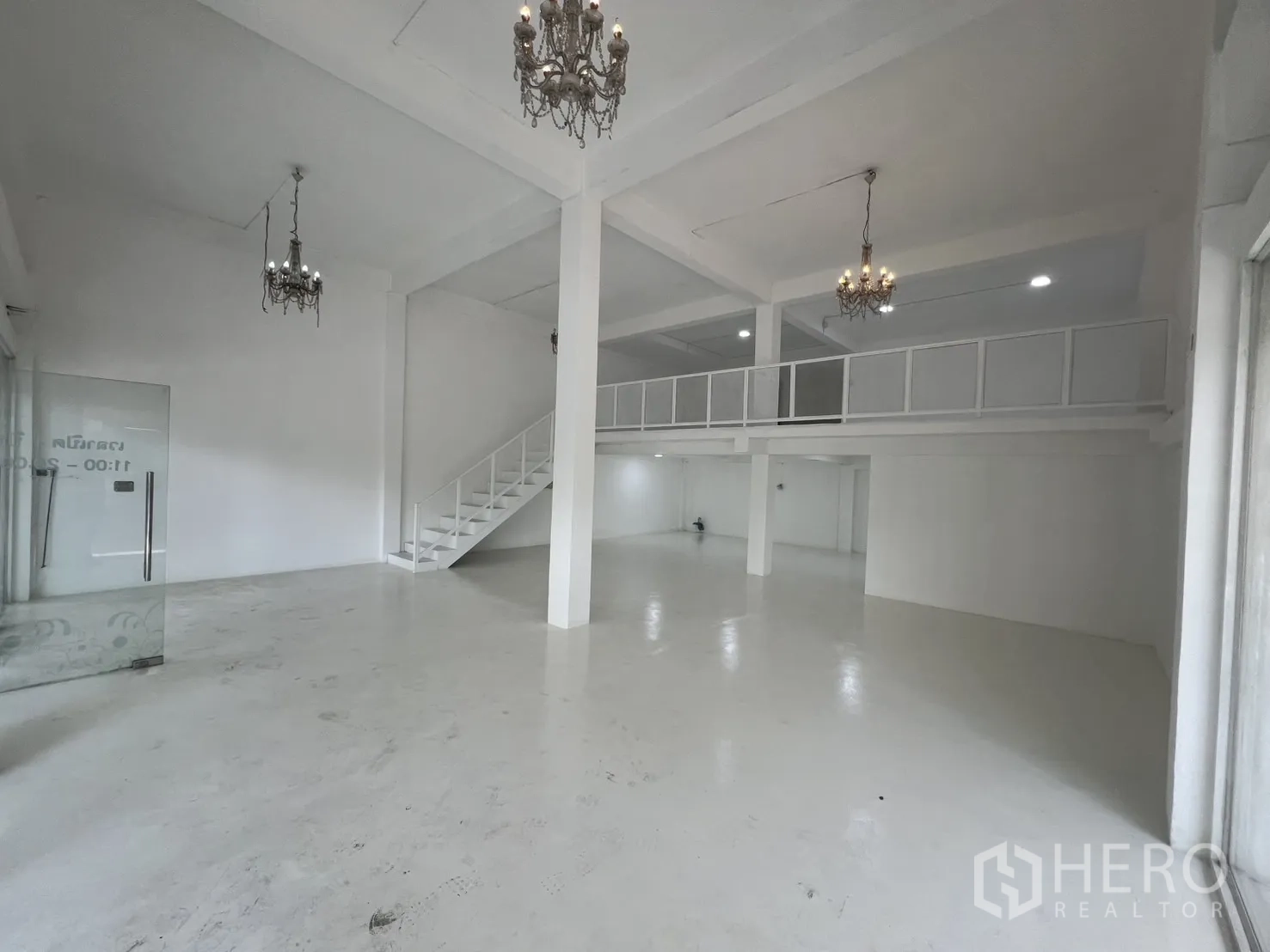 Retail Space for rent in Khlong Toei, Bangkok - Open-plan white retail interior with double-height ceiling, mezzanine and chandeliers.