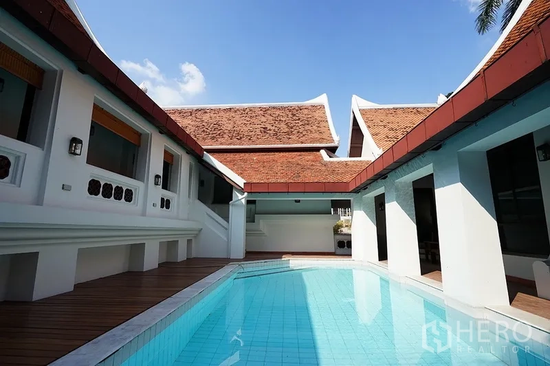 独立式住宅 出租在Watthana, Bangkok - 庭院视角的泳池，四周为传统山墙屋顶，天空晴朗。